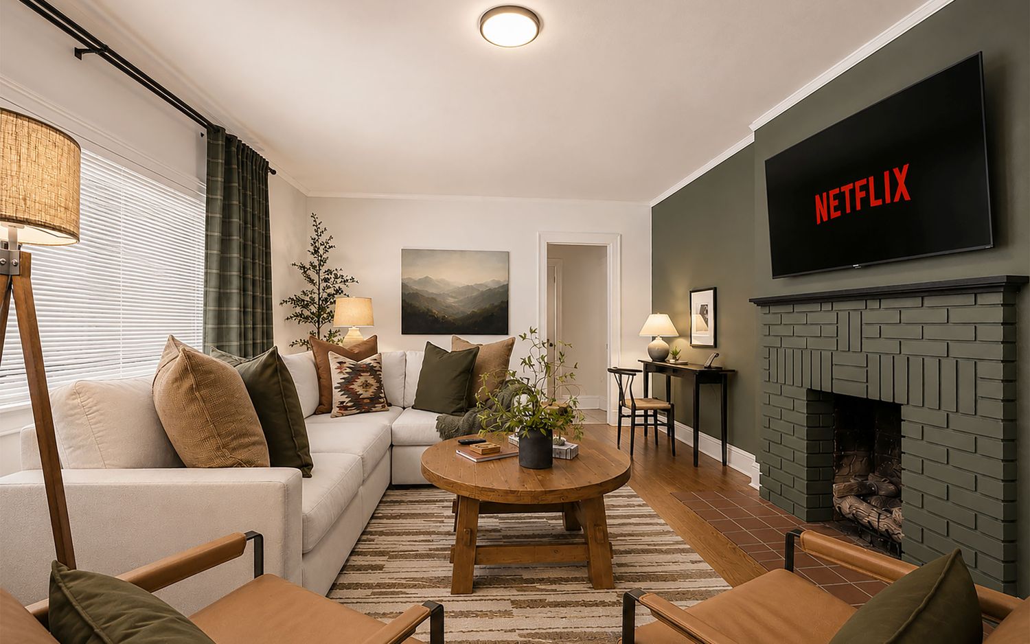 Living room at Maple & Main with a deep green painted fireplace, linen sectional and round wood coffee table