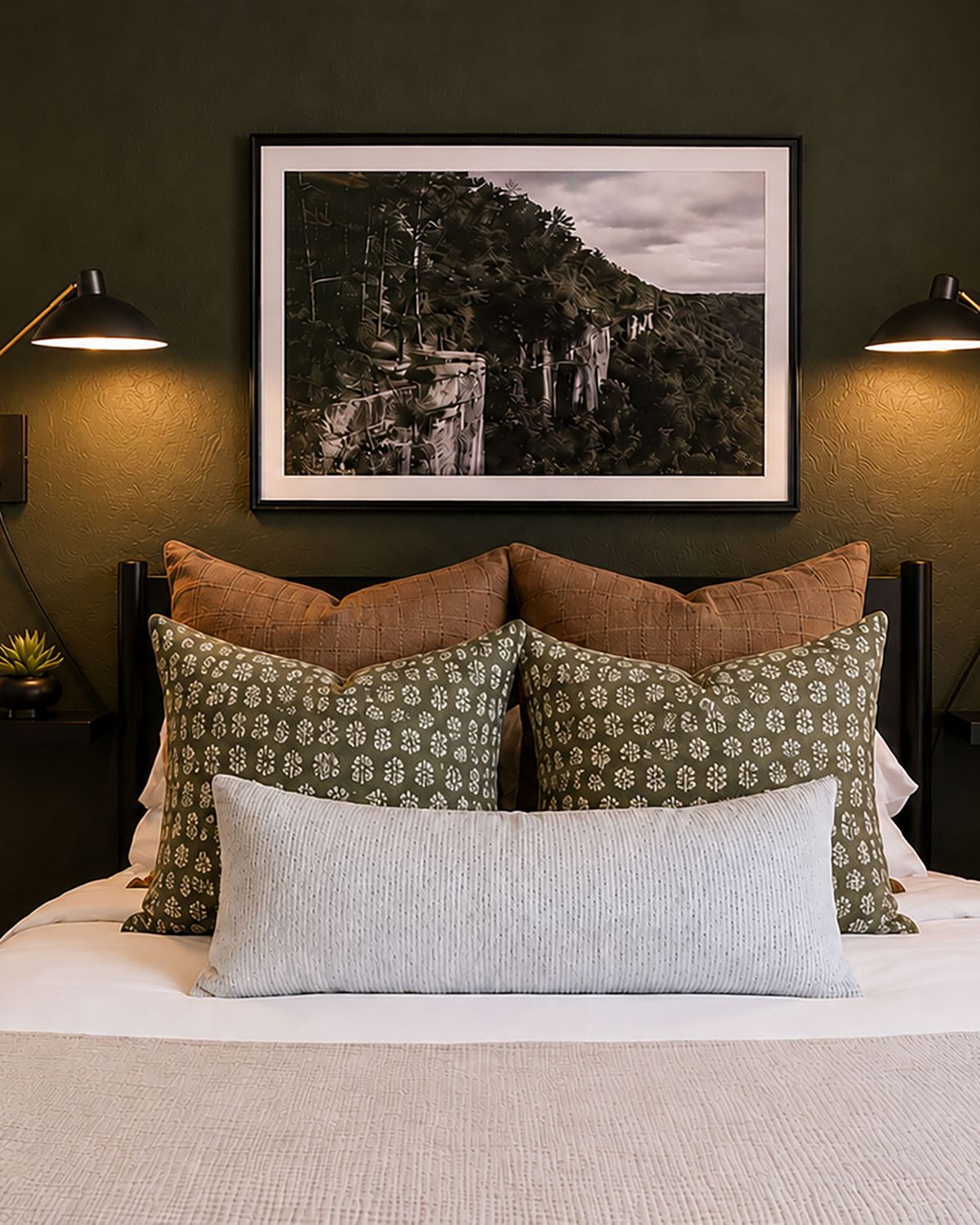 Queen bedroom with a deep green accent wall, sconces and layered pillows