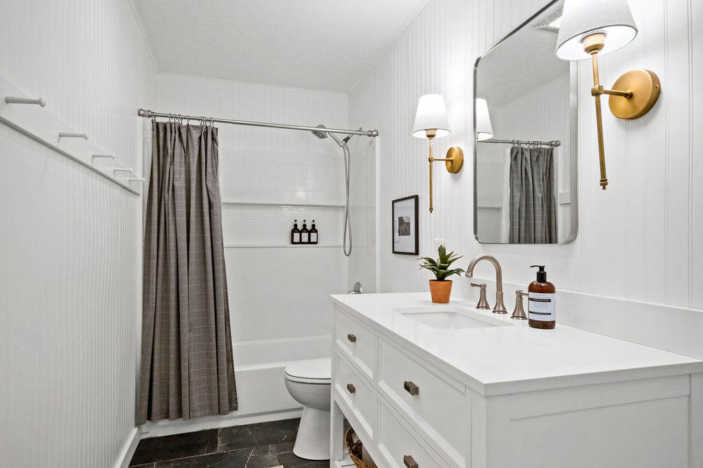 Gorge Getaway bathroom today with white vanity, brass sconces and tiled tub